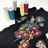 A table with several different colored thread and some flowers.
